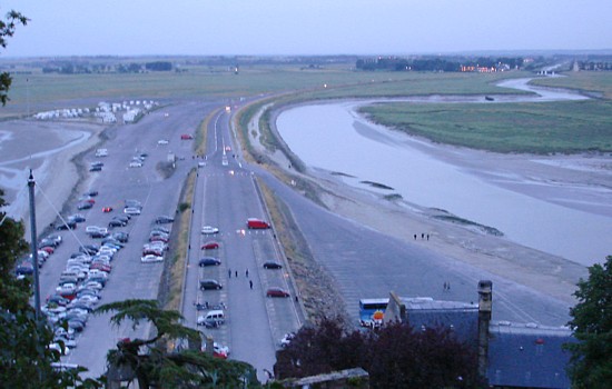 Mont-Saint-Michel am Tor zur Bretagne -  Blick auf den Damm mit Parkplätzen und die versandete Mündung des Couesnon mit Salzweiden und altem Wehr im Hintergrund.